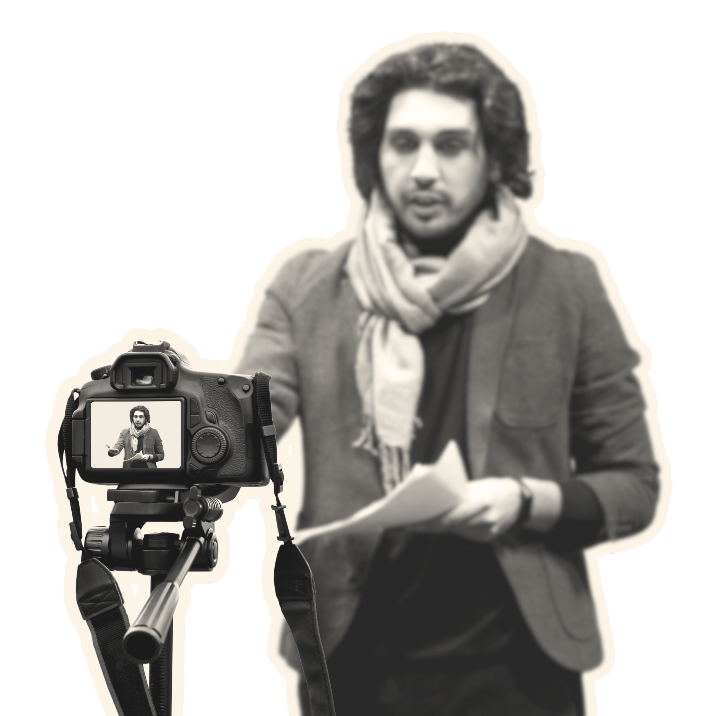 A man with curly hair and a scarf stands in front of a camera on a tripod, holding a paper, being recorded or photographed.