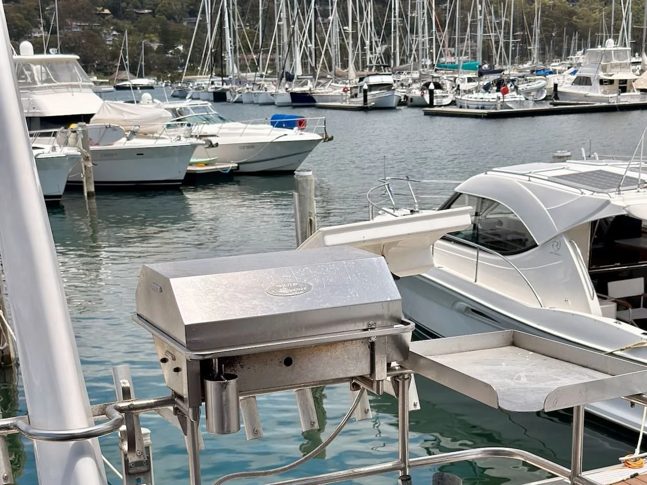 Marina with multiple moored boats and yachts, with a stainless steel grill and tray in the foreground.