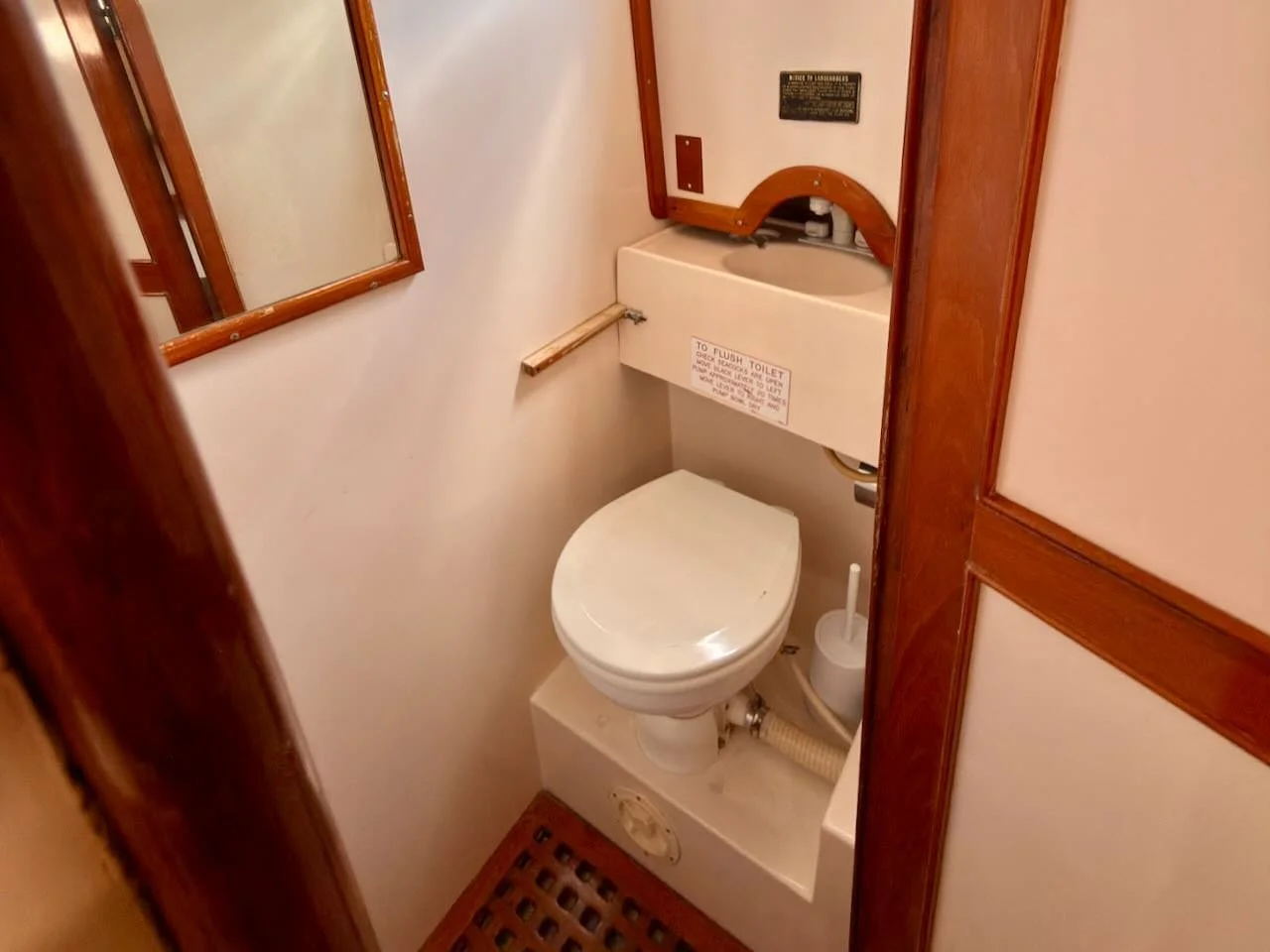 Small boat bathroom with a toilet, a small sink, a mirror, and wooden accents.