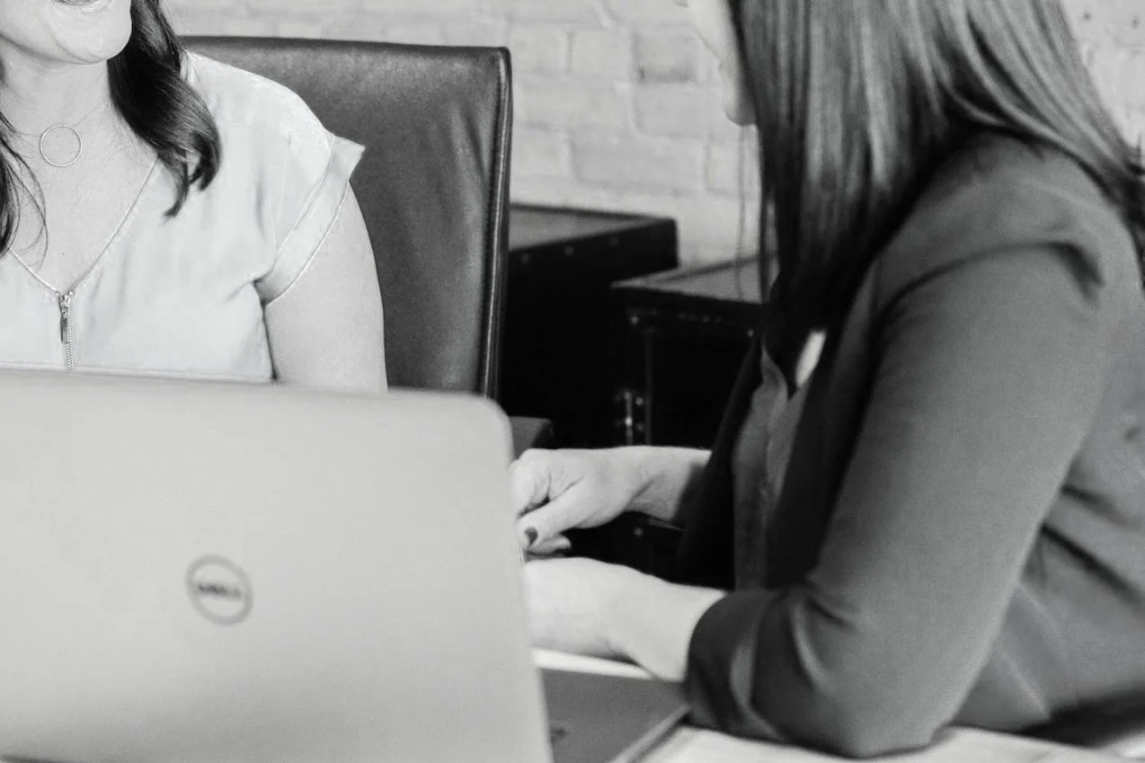 Two people sitting at a desk, working on a Dell laptop, in a professional setting.