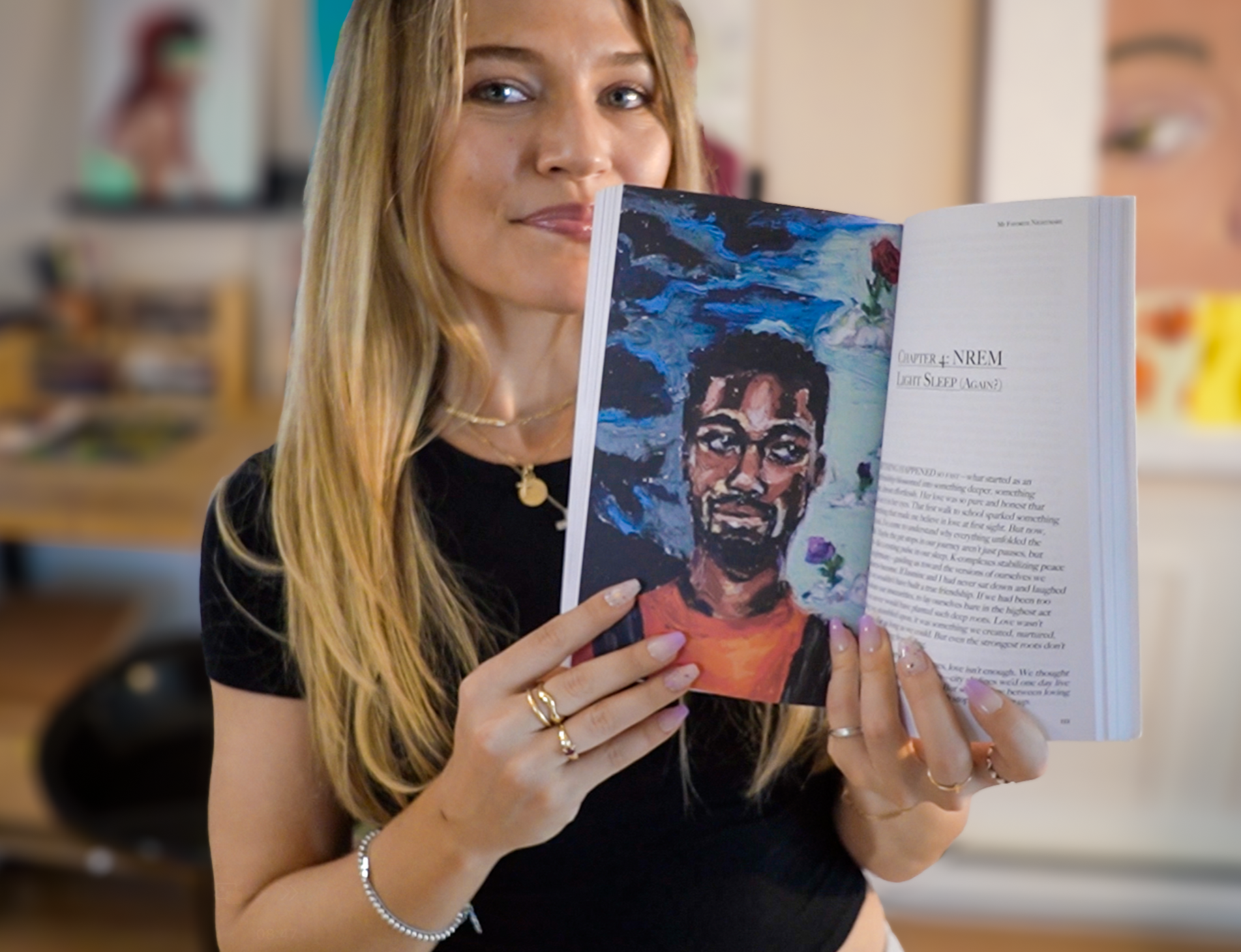 A woman with long blonde hair, wearing a black shirt, holding a colorful illustrated book open to a page with a portrait that she drew in oil pastel, in her studio.