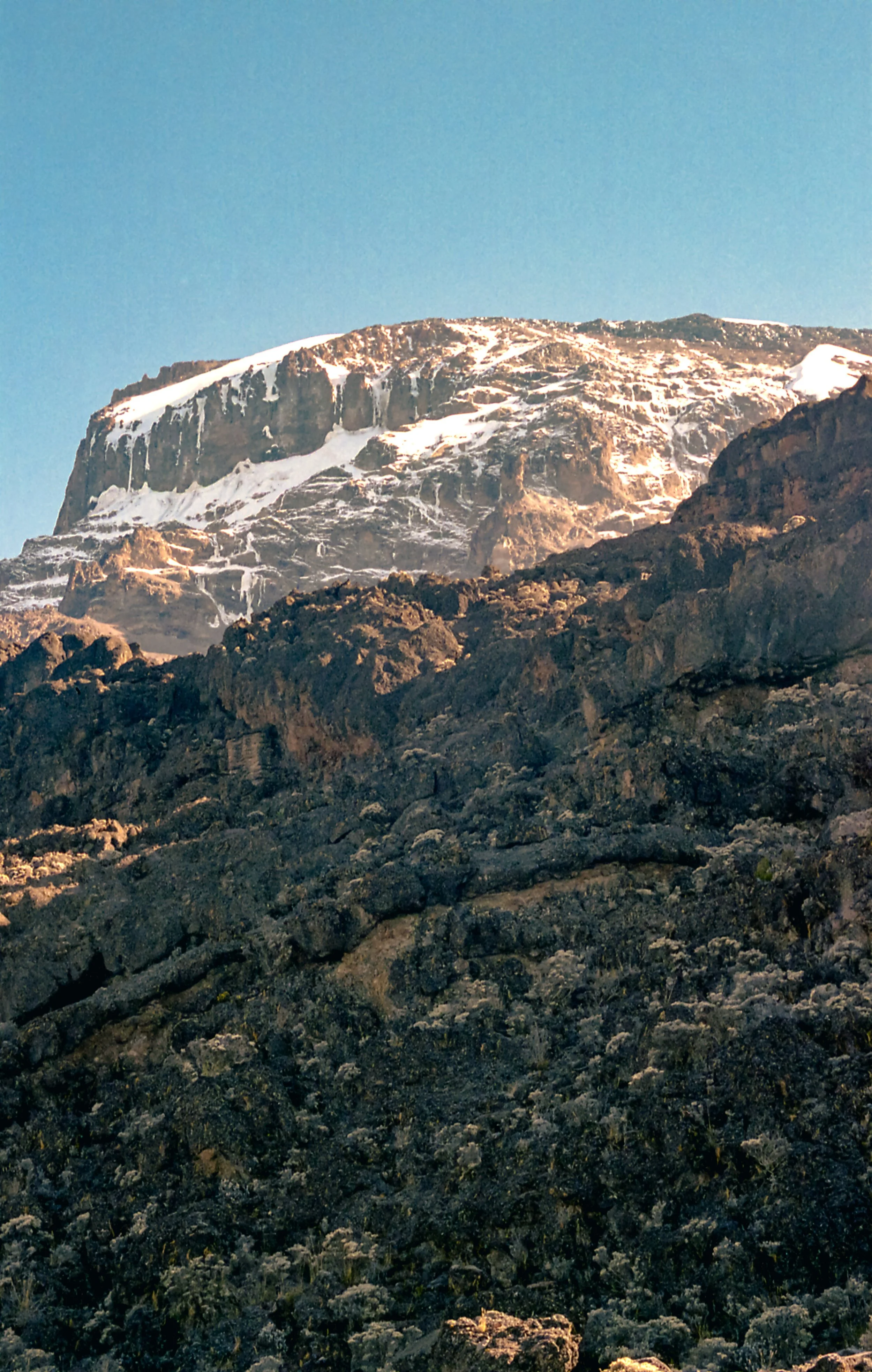 Mountain peak with snow caps and rugged terrain under a clear blue sky.