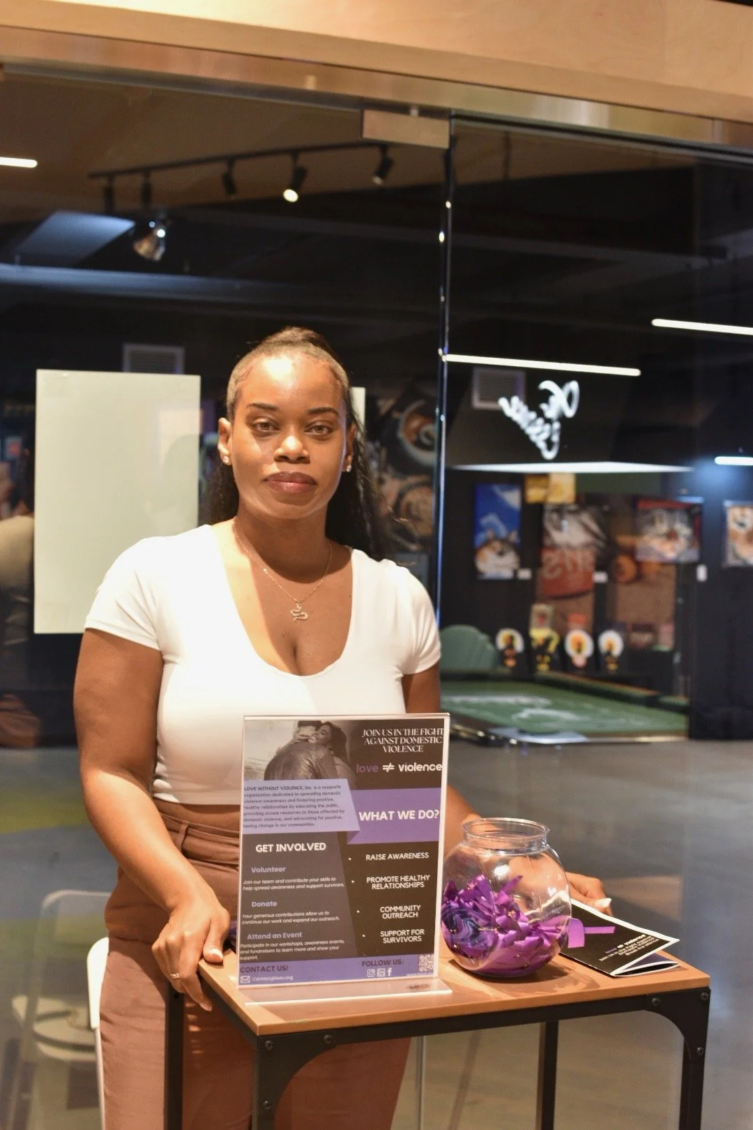 Woman standing behind a table with informational flyers about fighting domestic violence, next to a jar of purple ribbons.