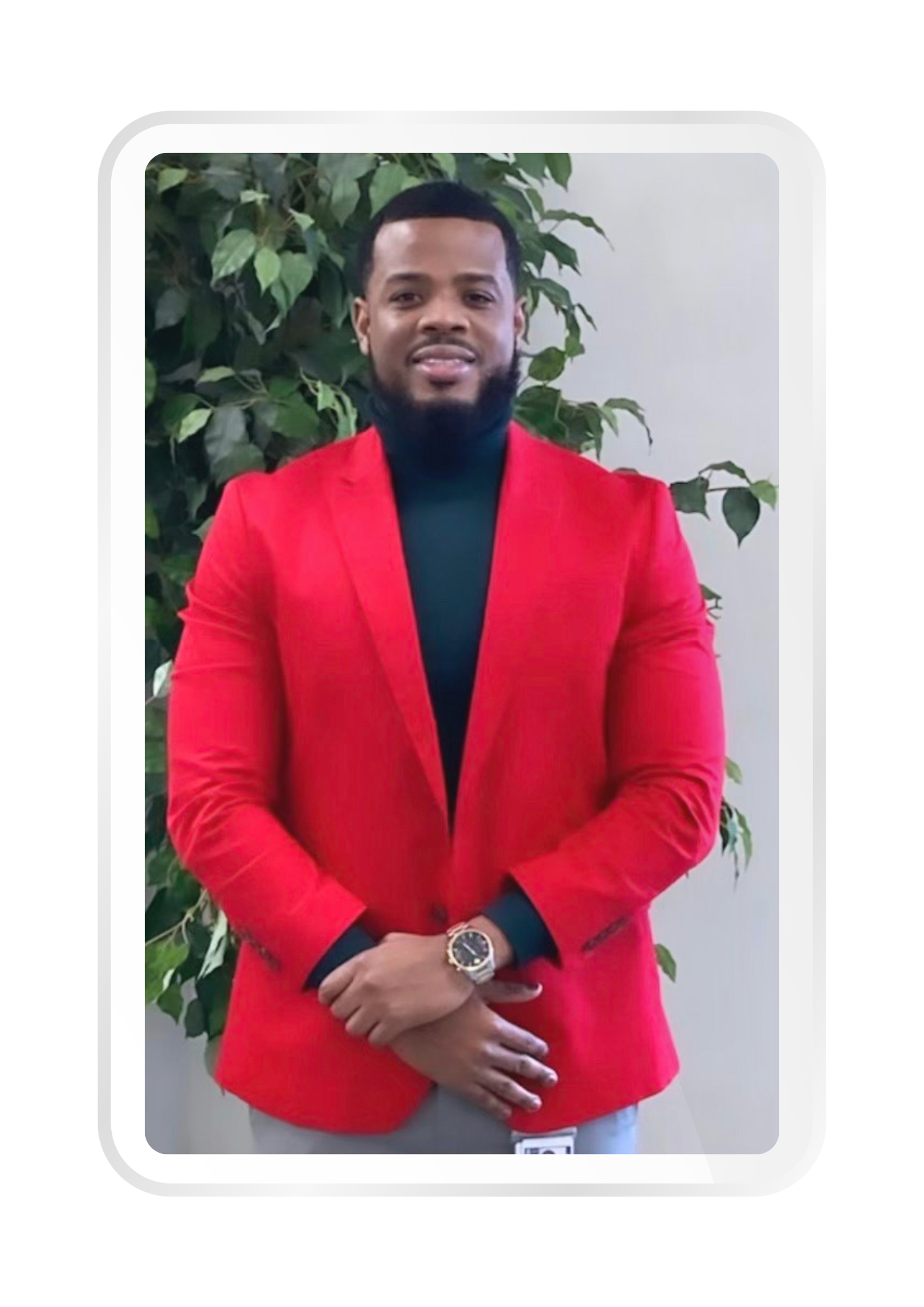 Man in a red blazer standing in front of a leafy plant, smiling.