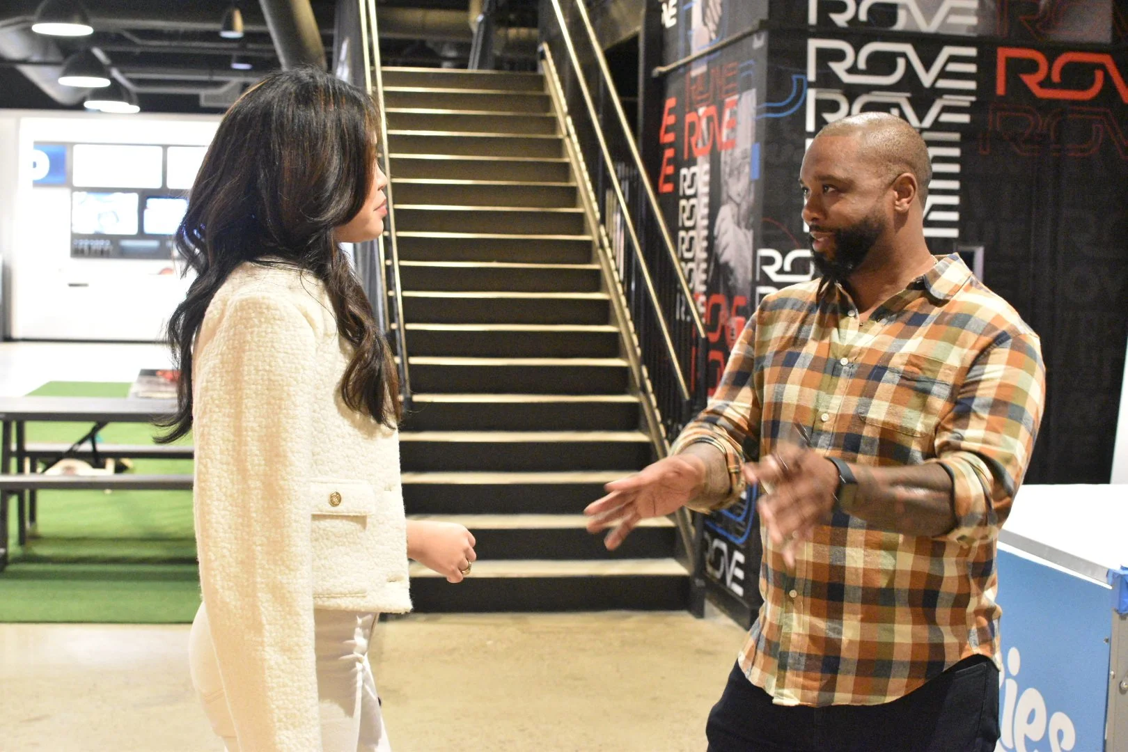 Two people having a conversation near a staircase in an indoor setting with modern decor.