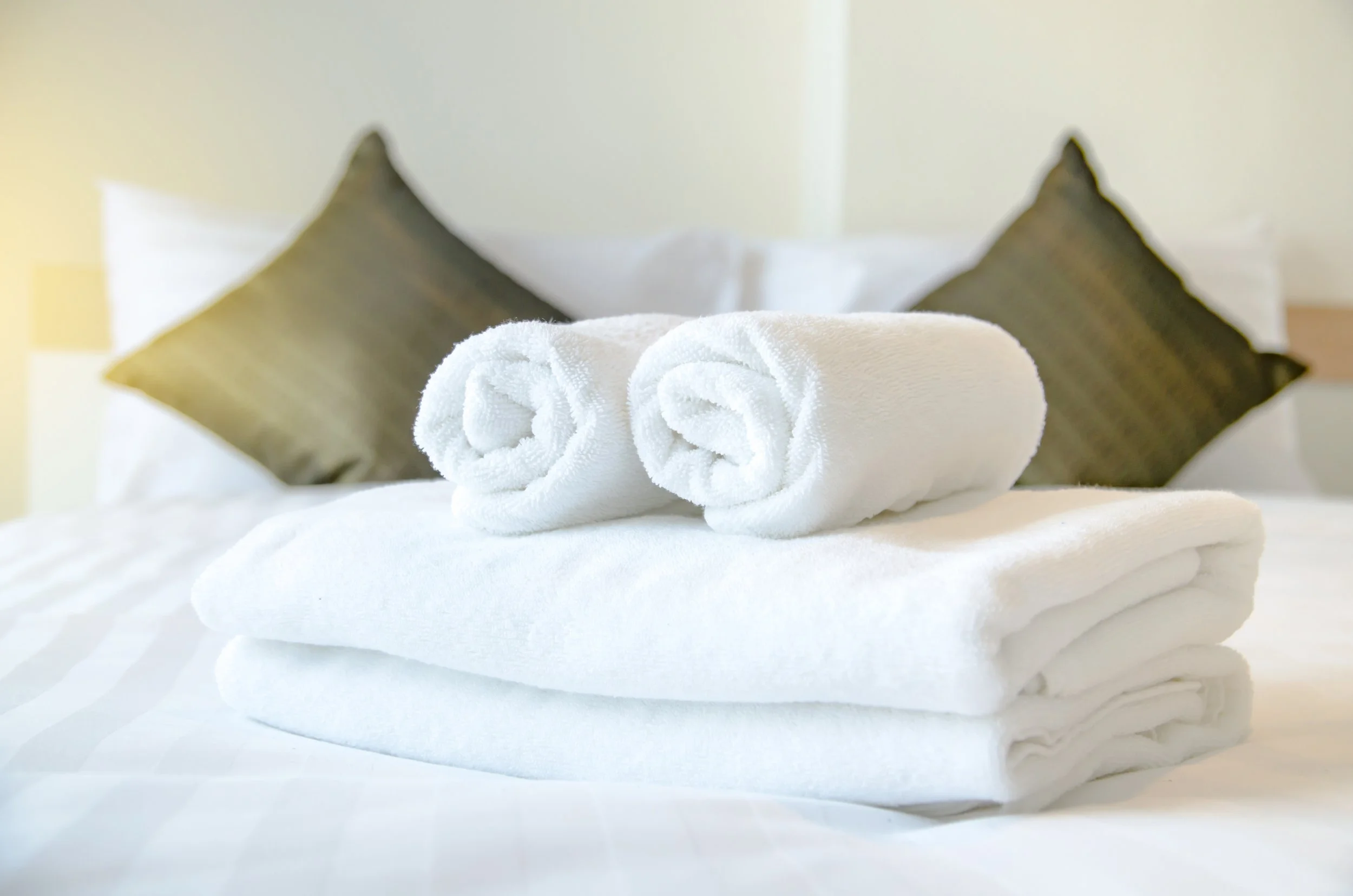 Rolled white towels stacked on a hotel bed with pillows.