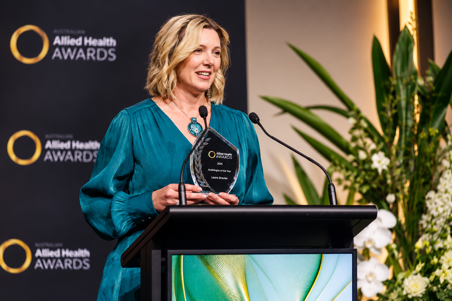 Laura Drexler speaking at the 2026 Allied Health Awards while holding her Audiologist of the Year award