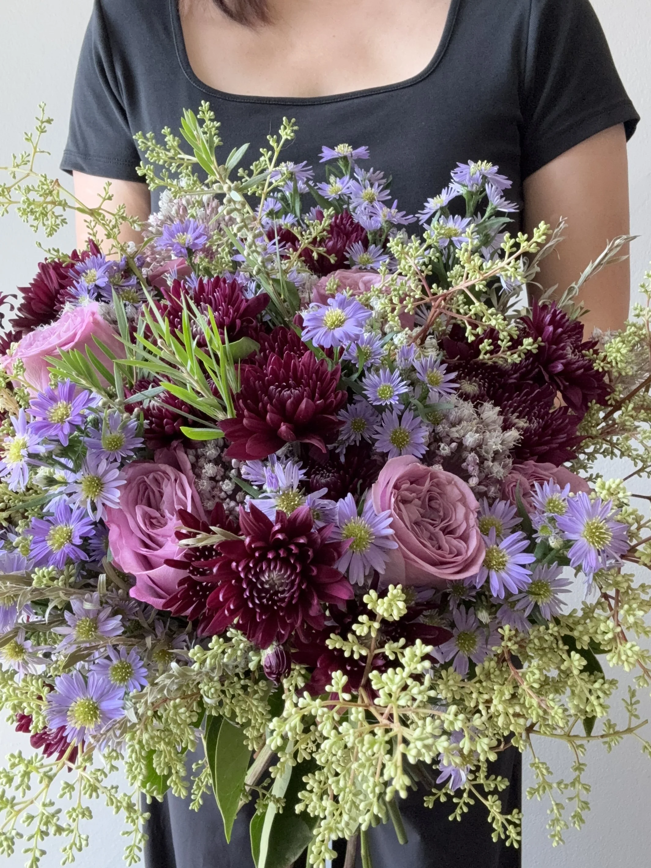 Moody purple and burgundy floral arrangement in hand