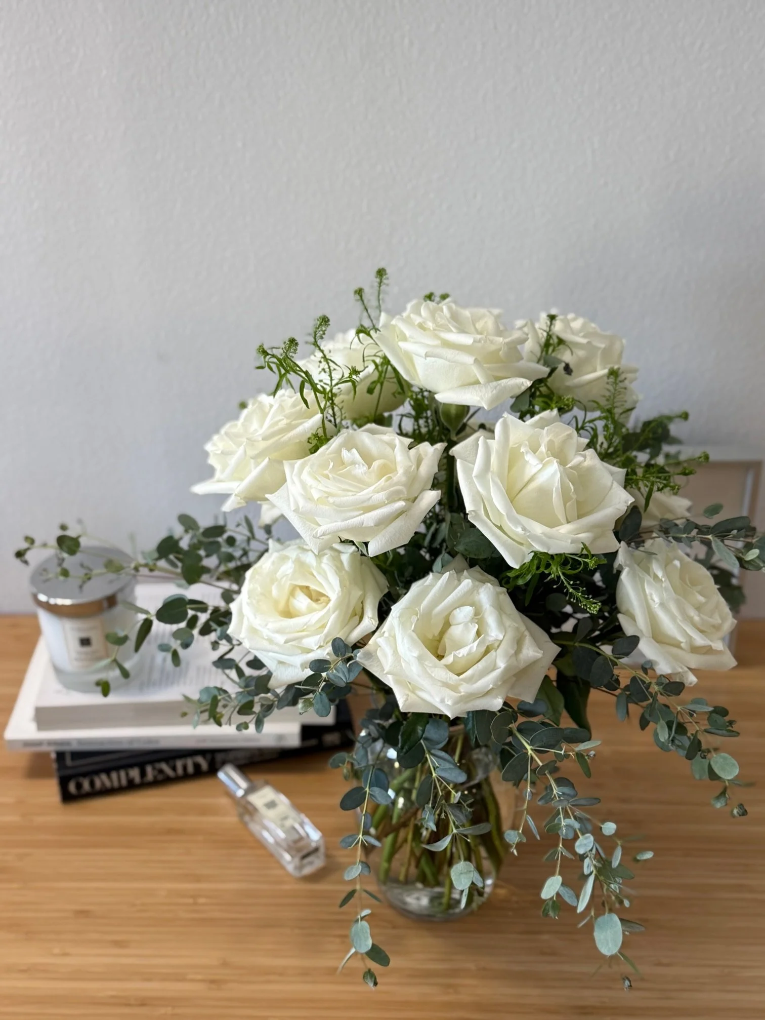 Classic white roses with eucalyptus in a clear glass vase, styled for home décor on a wooden table — Girl and the Flower, Los Angeles.jpeg
