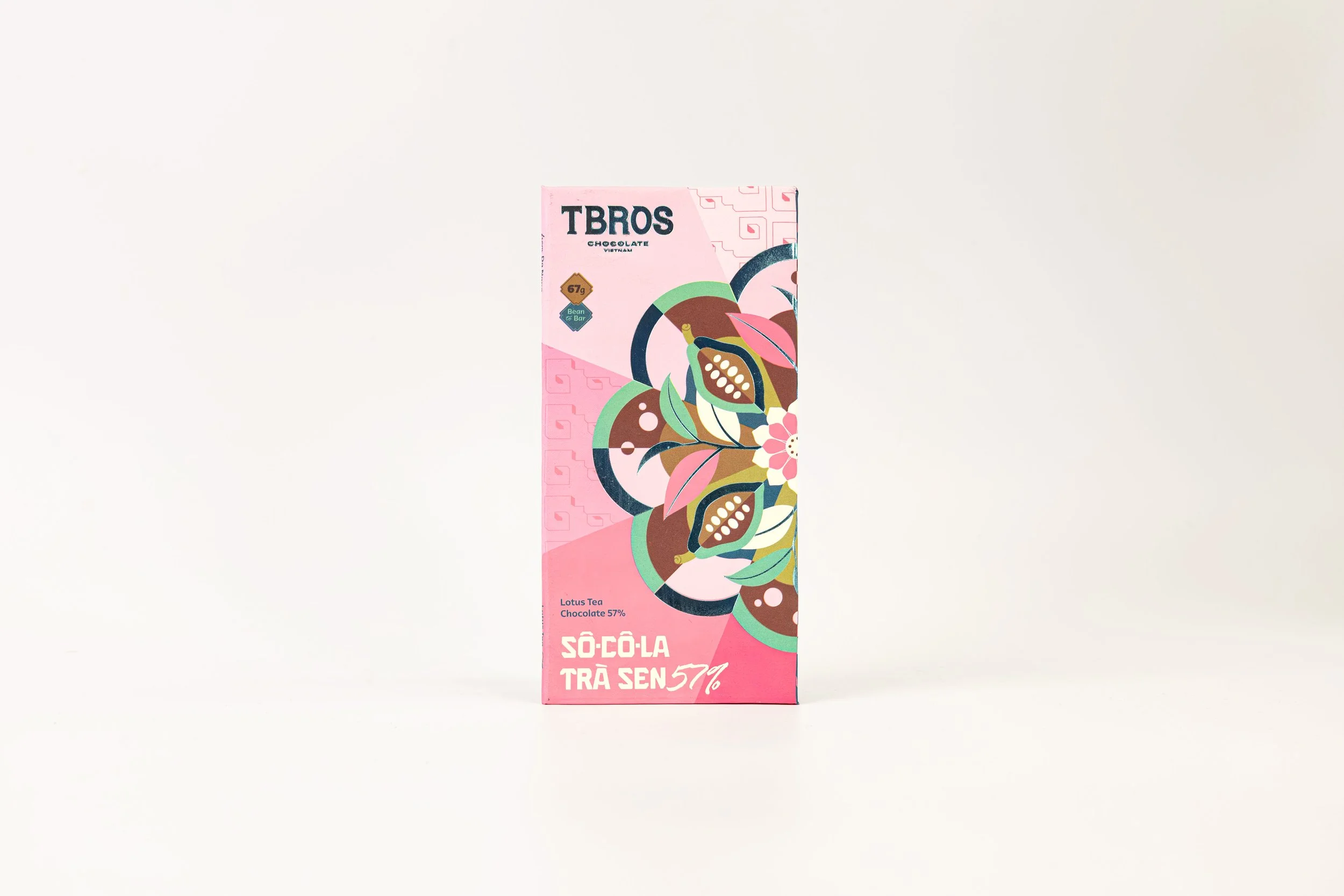 Pink box of TBROS chocolate with colorful abstract floral design, ingredients note of lotus tea and 57% cacao content, placed on a white background.