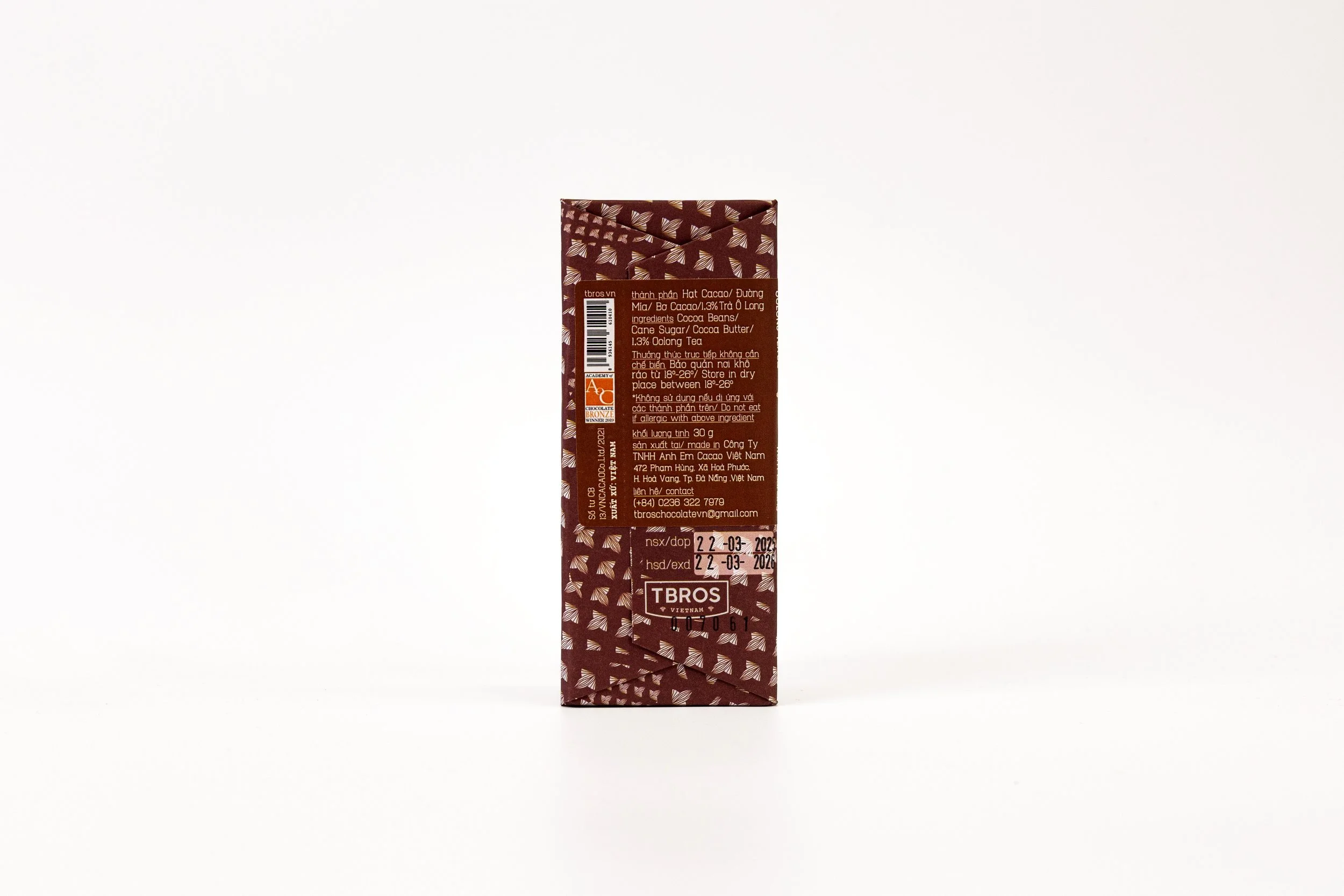 Back of a chocolate bar packaging with a brown and patterned design, featuring text in Vietnamese and English, including a barcode, expiration date, and manufacturer contact information.