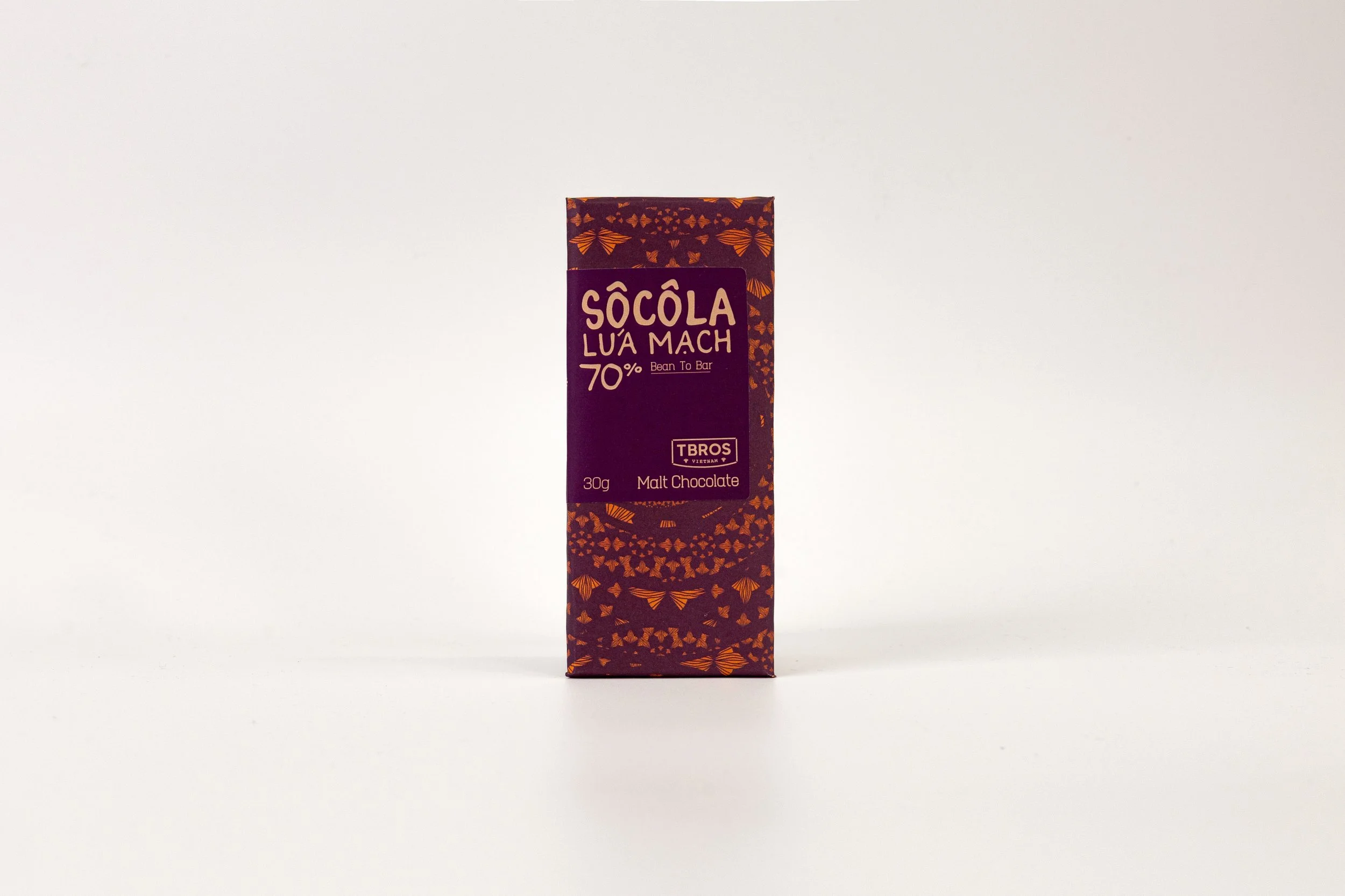 A chocolate bar in purple packaging with orange leaf and butterfly patterns, labeled 'Socola Lua Mach 70% Bean To Bar, Malt Chocolate, 30g, TBROS, Vietnam' on a plain white background.