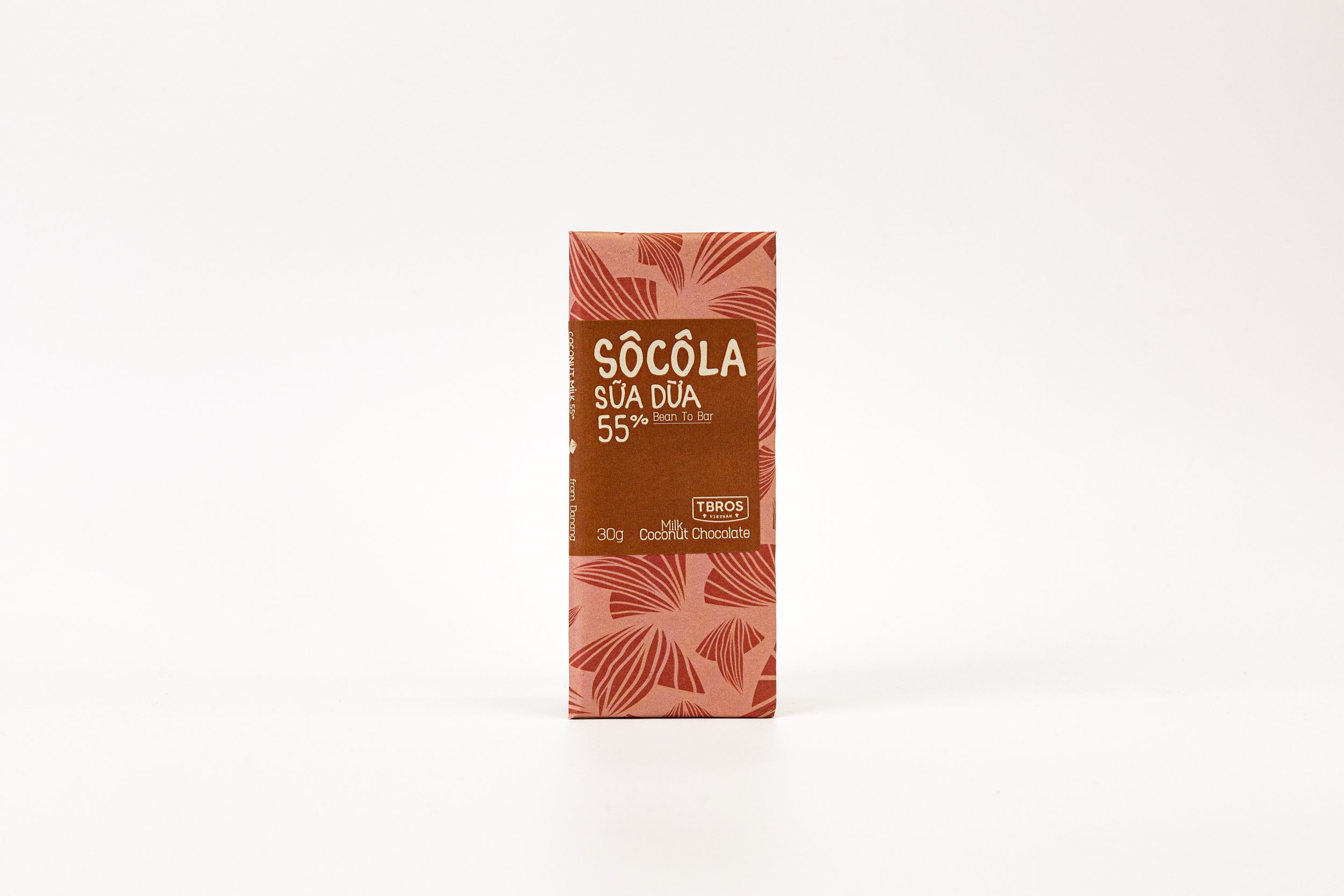 A pink rectangular chocolate bar with tropical leaf patterns, labeled 'Sôcôla Sữa Dừa 55%' and 'Bean To Bar,' with additional information including 'Milk Coconut Chocolate' and '30g'.