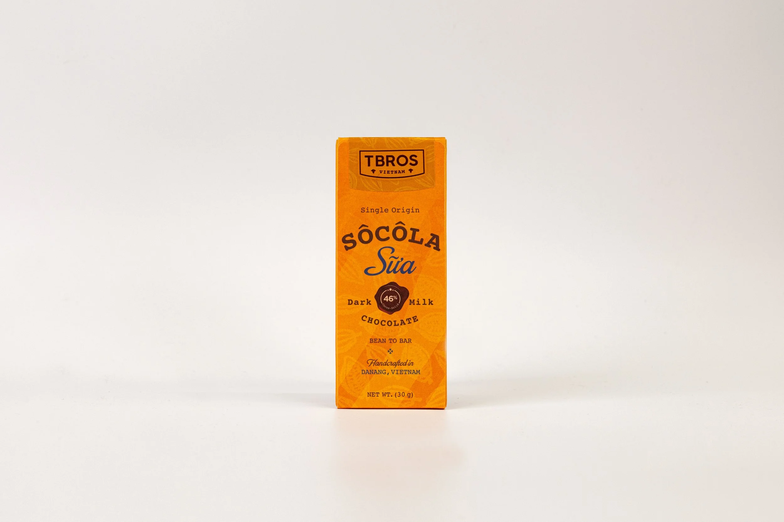 A tall, orange chocolate bar packaging with black and blue text, labeled 'Sôcôla Sữa' indicating milk chocolate, and details about the origin, ingredients, and weight.