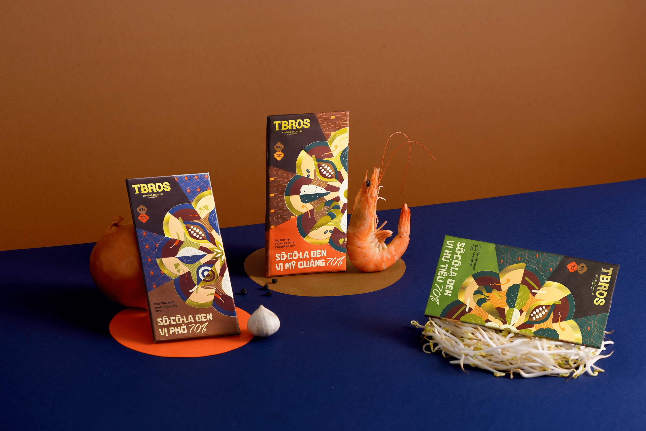 Assorted dark chocolate bars with colorful packaging, a raw shrimp, garlic, bean sprouts, and an onion arranged on a blue and brown background.
