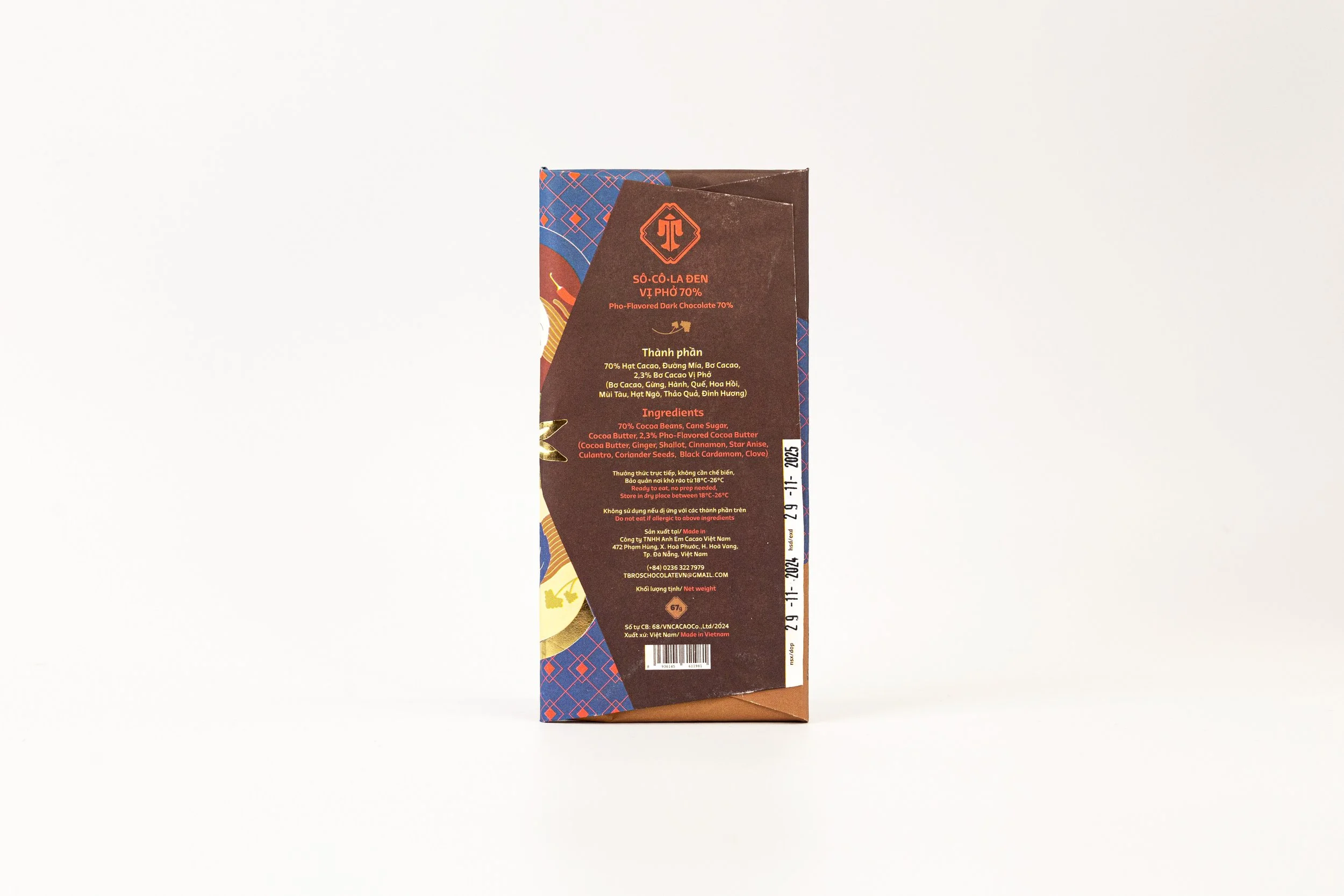 Side view of a chocolate bar package with a brown background and blue and red accents, showing ingredient and manufacturing information.