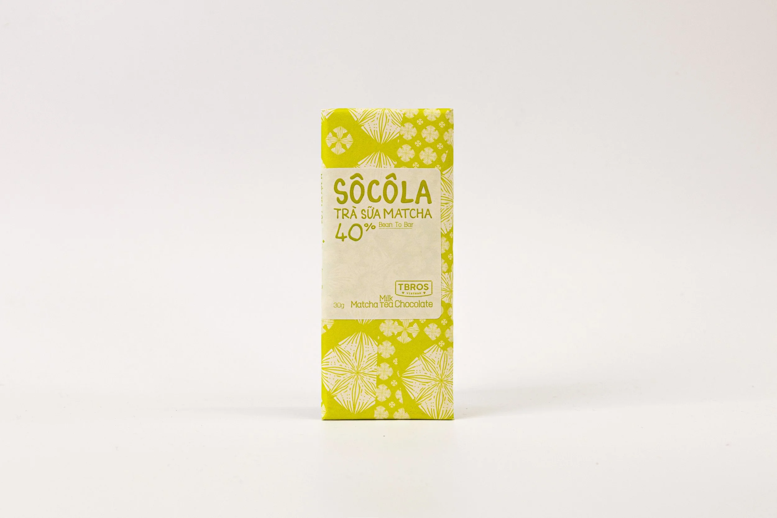 A yellow box of Socola Matcha milk chocolate with floral and geometric patterns, standing on a white surface against a white background.