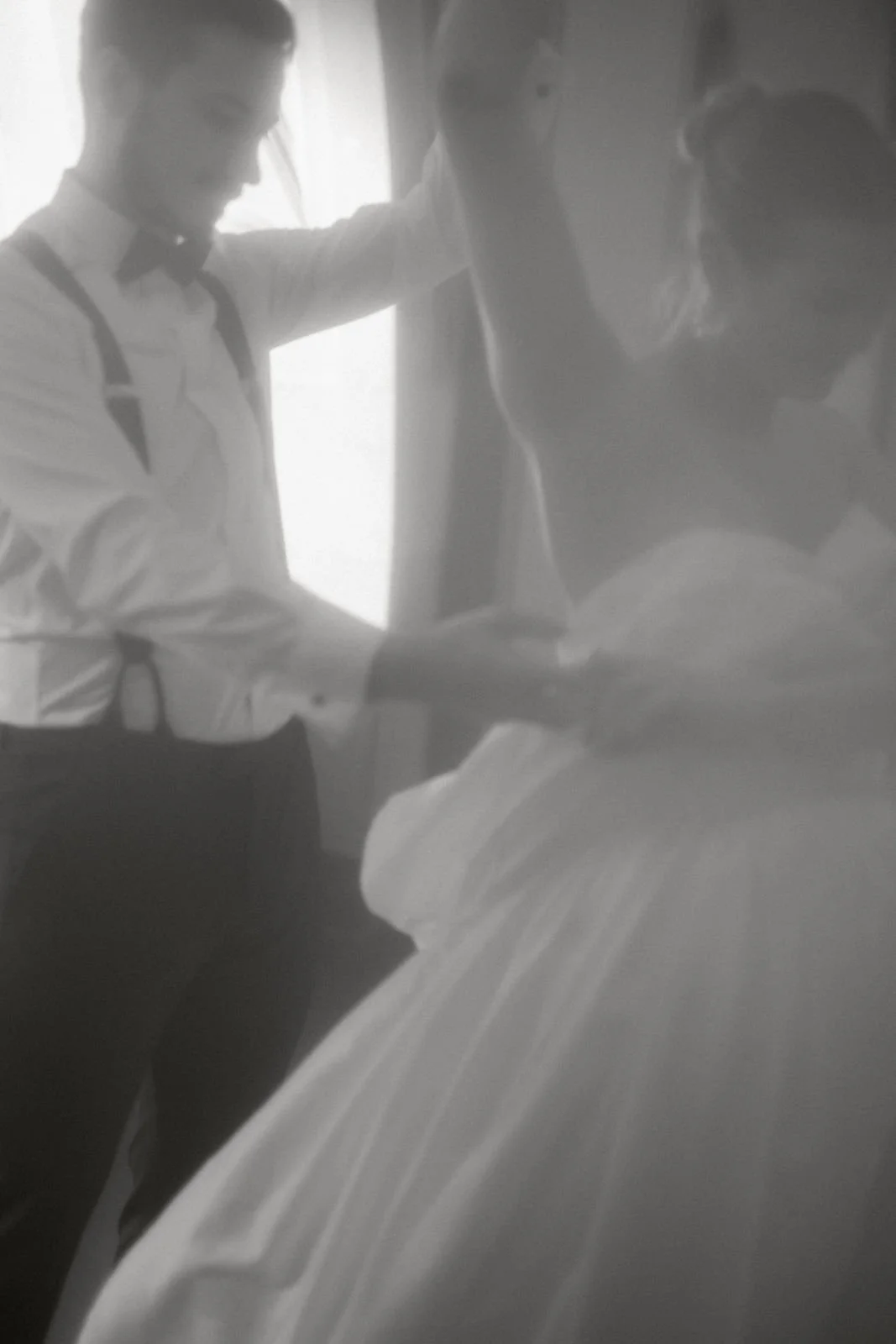 Zwei junge Männer, einer trägt eine weiße Hemd und eine schwarze Fliege, der andere trägt eine weiße Bluse, sie unterhalten sich in einem Raum mit natürlichem Licht.