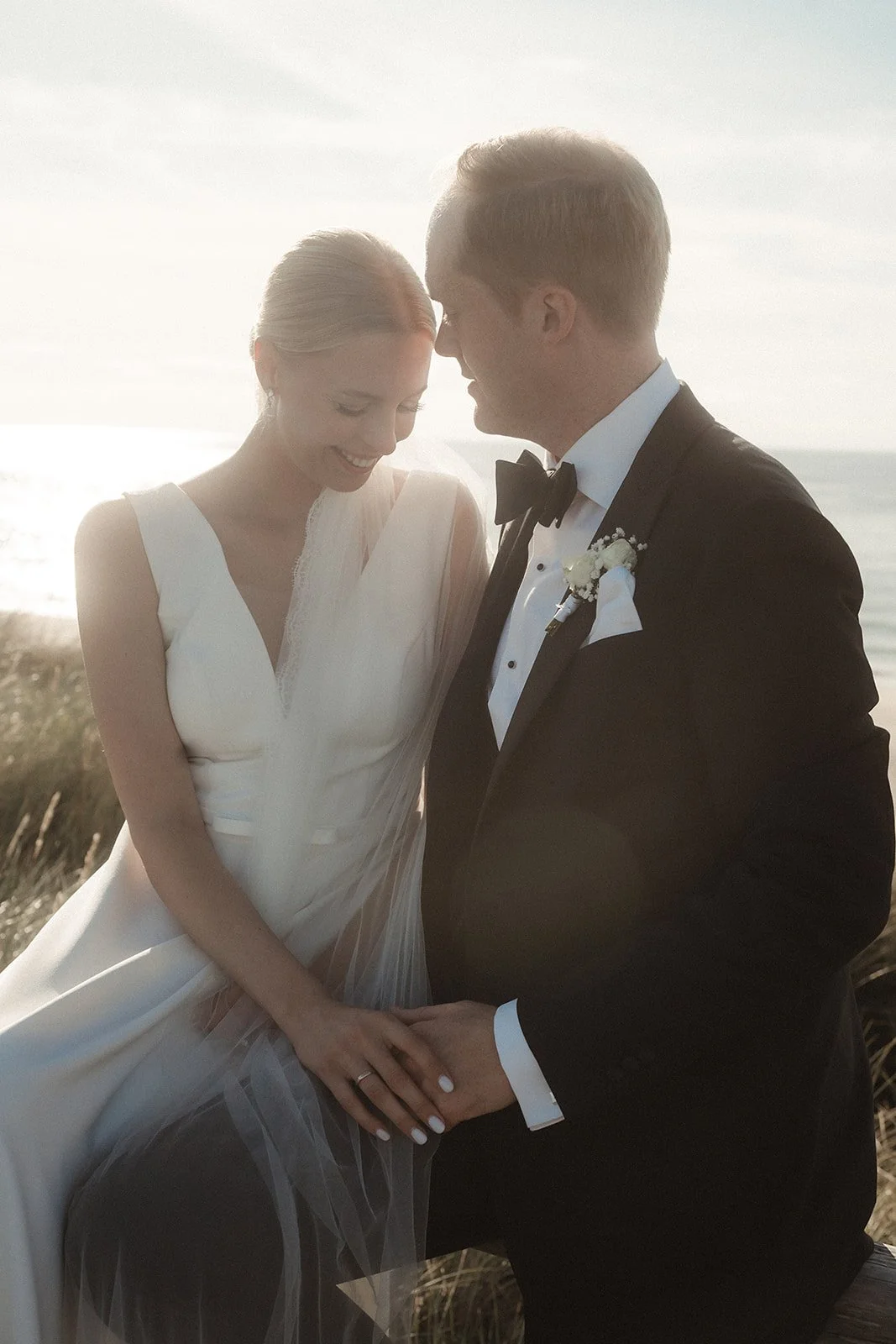 Ein brautpaar bei einer Hochzeit am Strand, das sich liebevoll ansieht und die Hände hält, bei Sonnenuntergang.