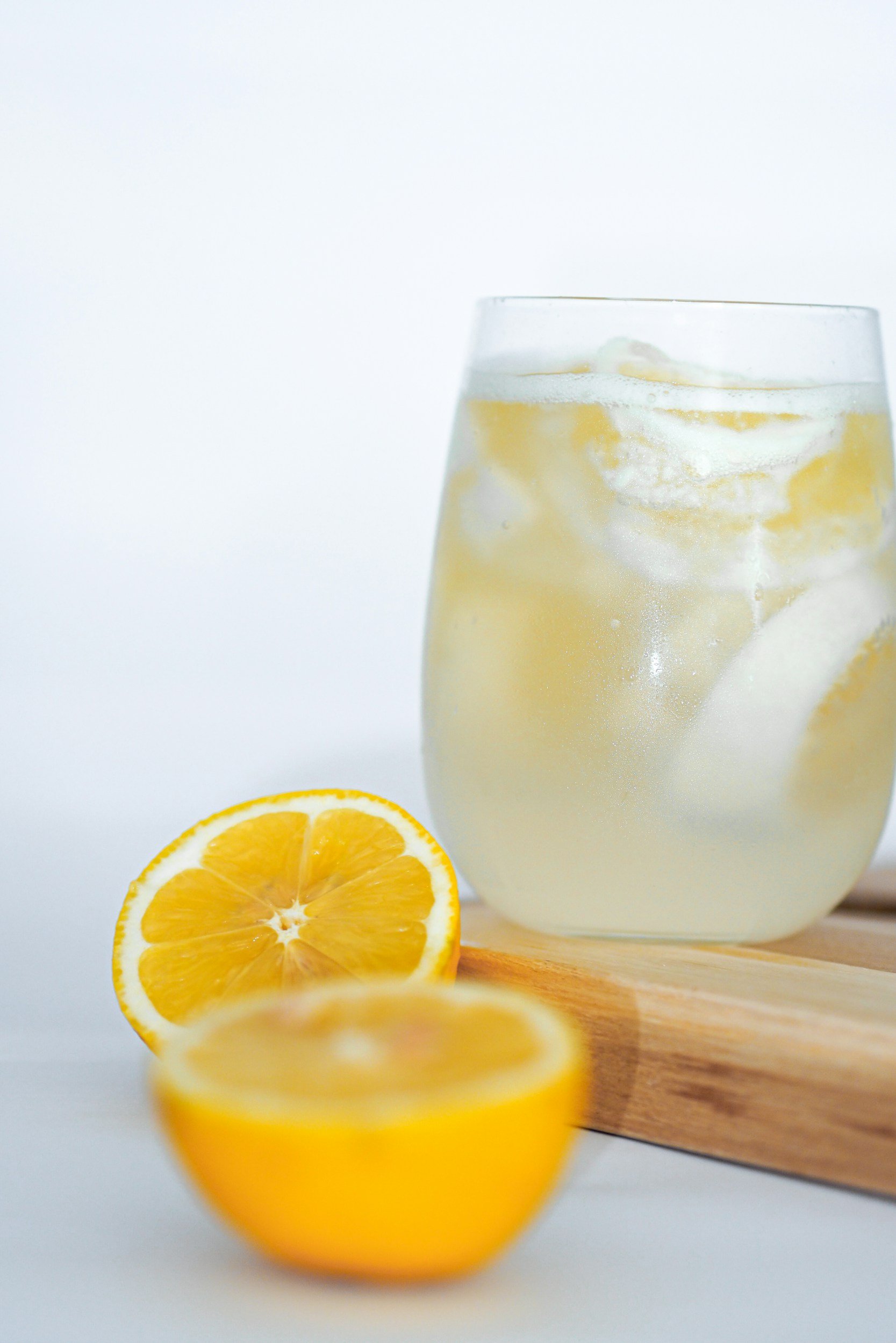 Et glas med lemonade og isterninger ved siden af en halveret citron og en hel citron.