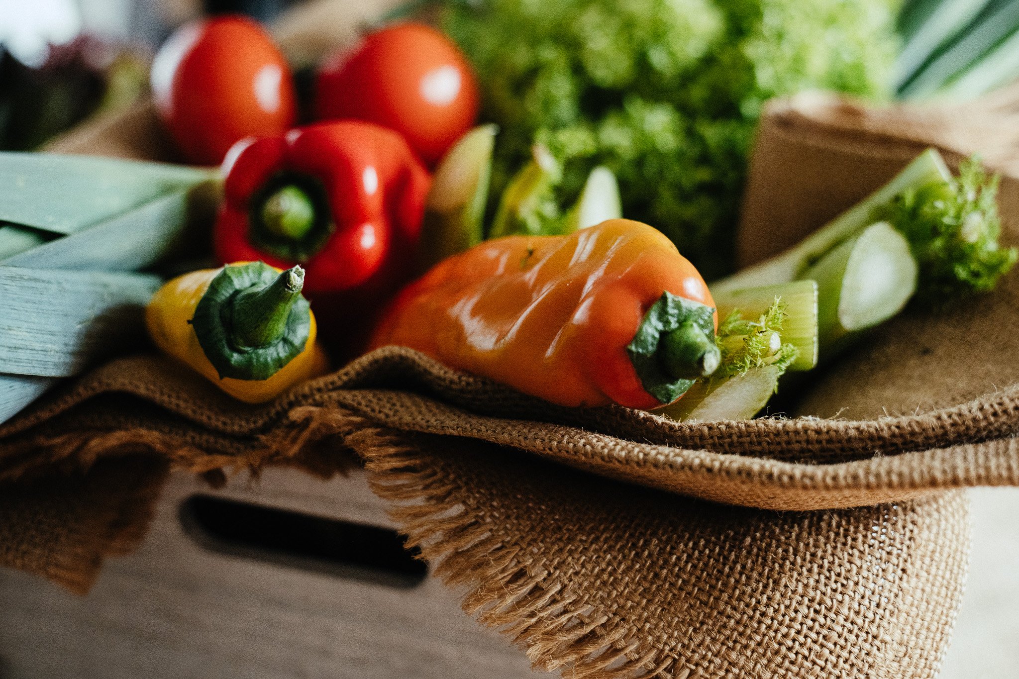 Frisches Gemüse wie Paprika, Tomaten und Salat in einem rustikalen Korb auf einem Leinentuch.