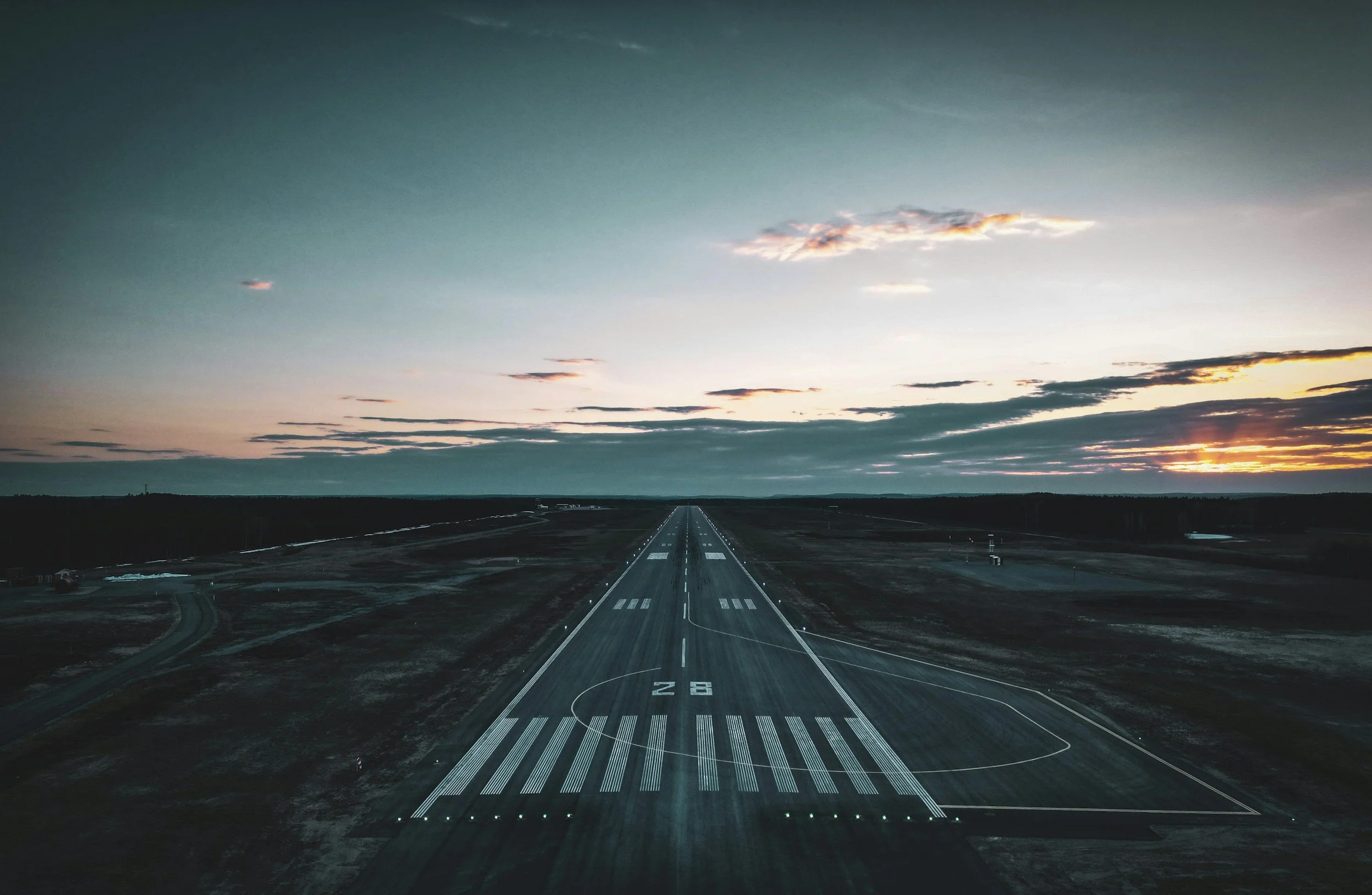 View of an empty runway and a sunset sky with scattered clouds.