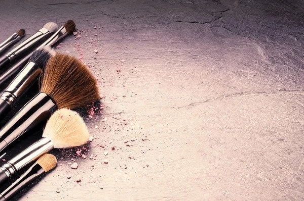 Collection of makeup brushes scattered on a textured surface with pink powder