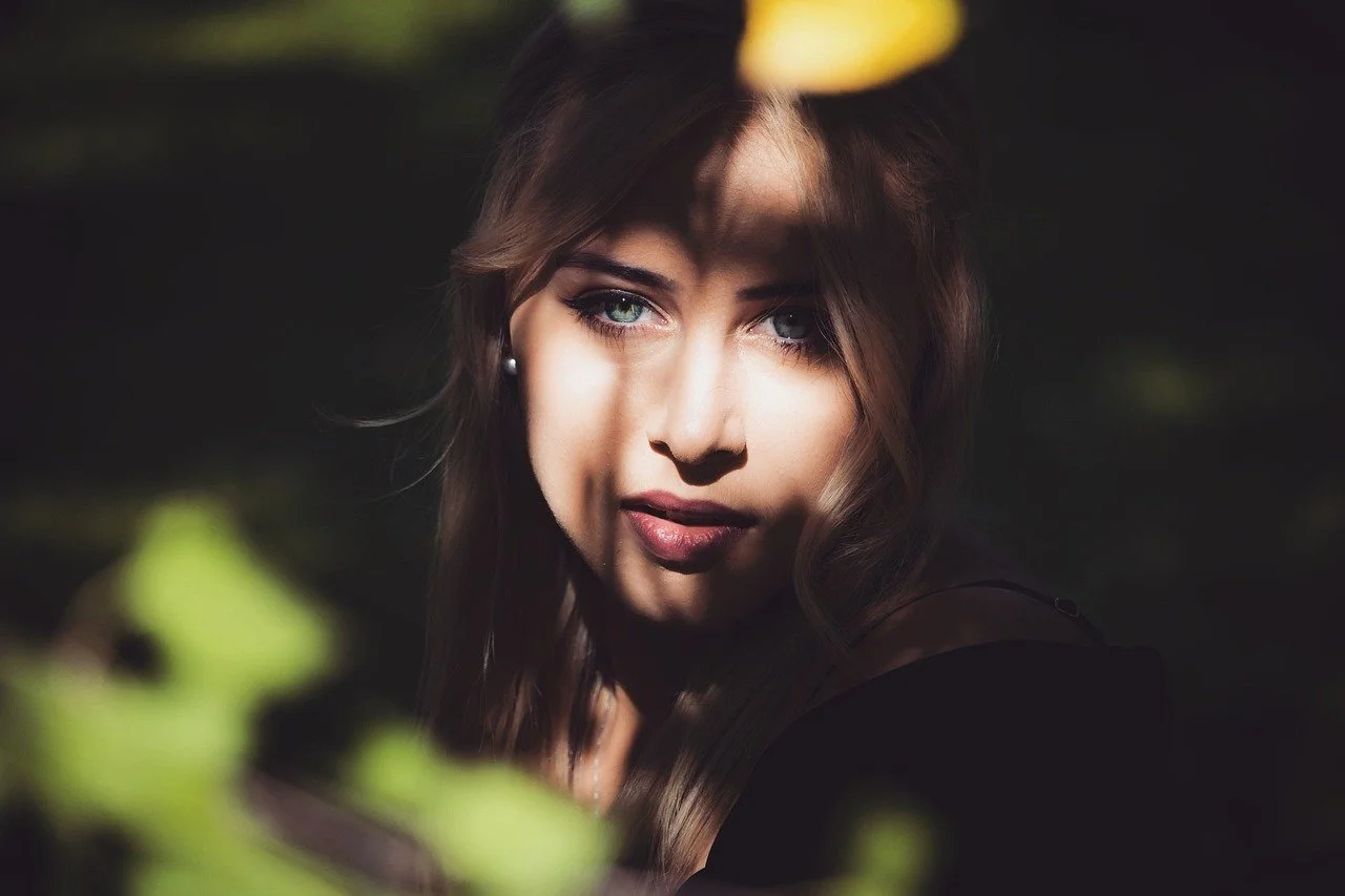 Close-up of a woman with green eyes and dark brown hair, looking directly at the camera with shadow and light patterns on her face.