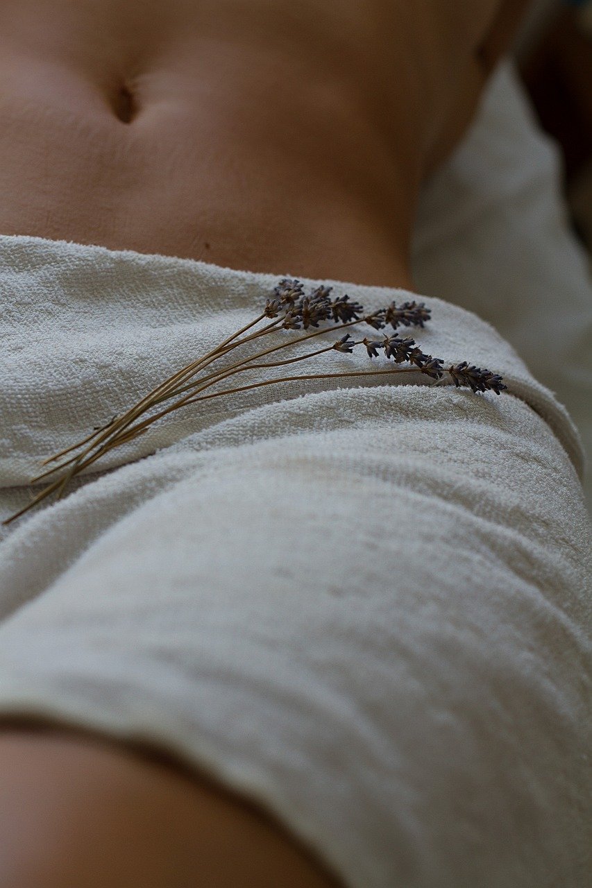 Close-up of a person's lower abdomen with lavender flowers resting on white fabric.