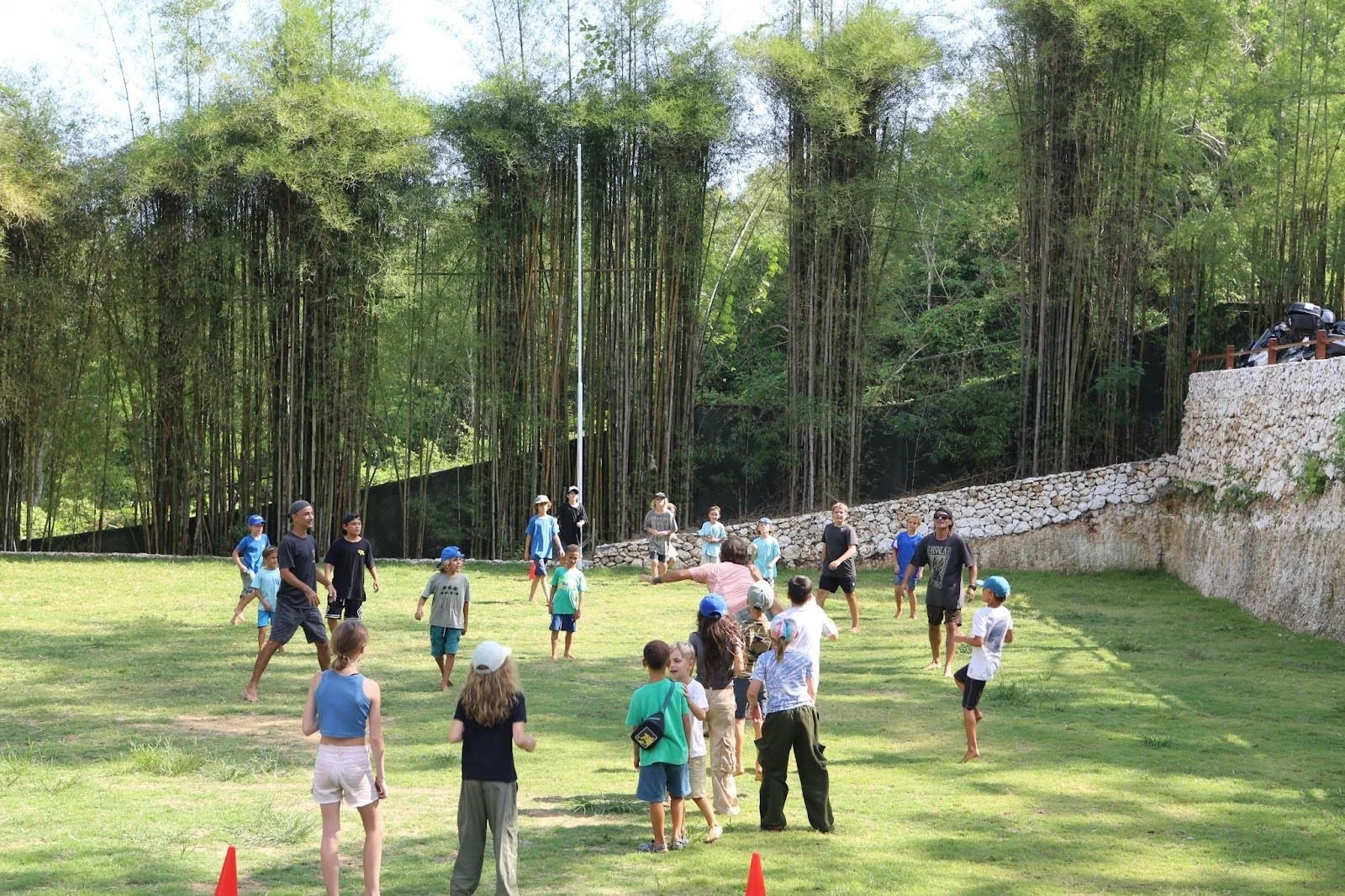 Students playing outdoor games in a grassy field surrounded by bamboo at Uluwatu School in Bali