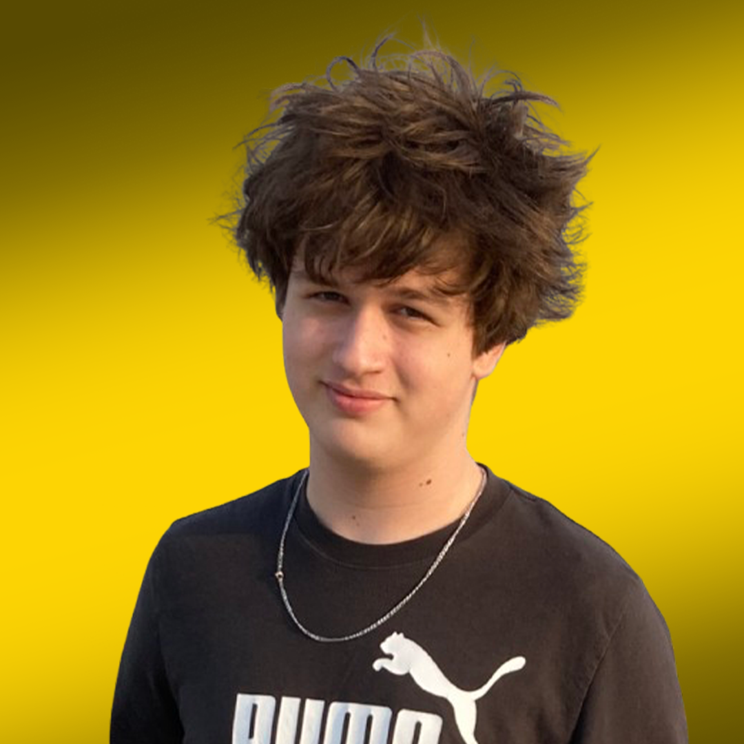 Young man with tousled hair smiling, wearing a black t-shirt and a chains, against a yellow background.