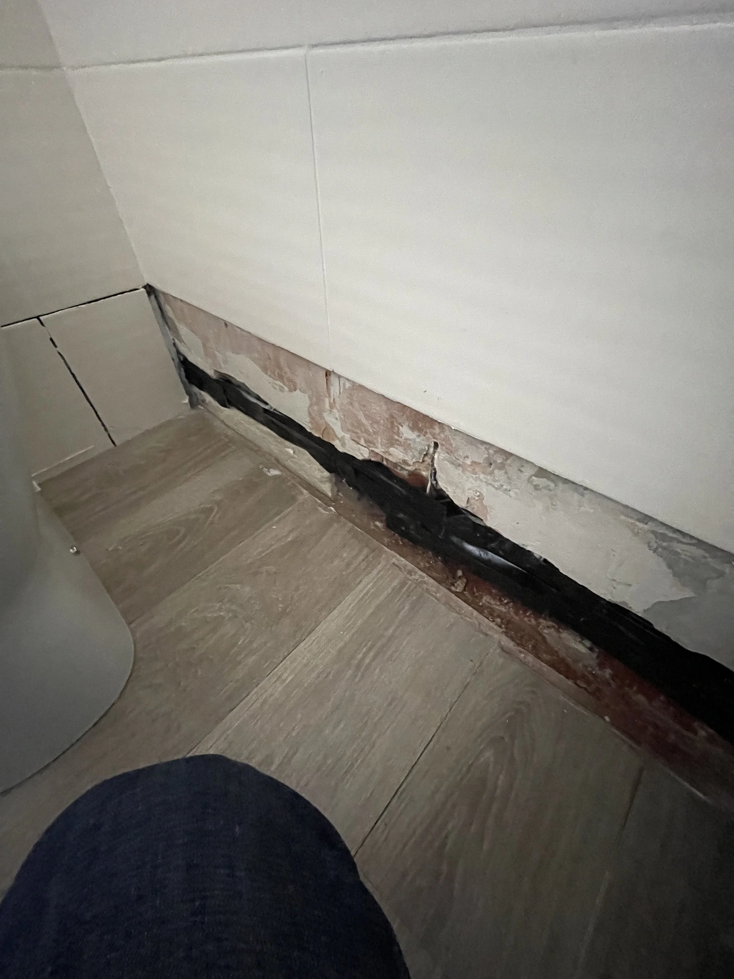 Bathroom wall with damaged tiles removed to expose the underlying surface during repair work.