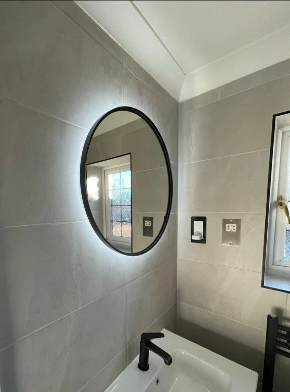 Contemporary bathroom with large-format porcelain tiles, illuminated mirror and premium black brassware.