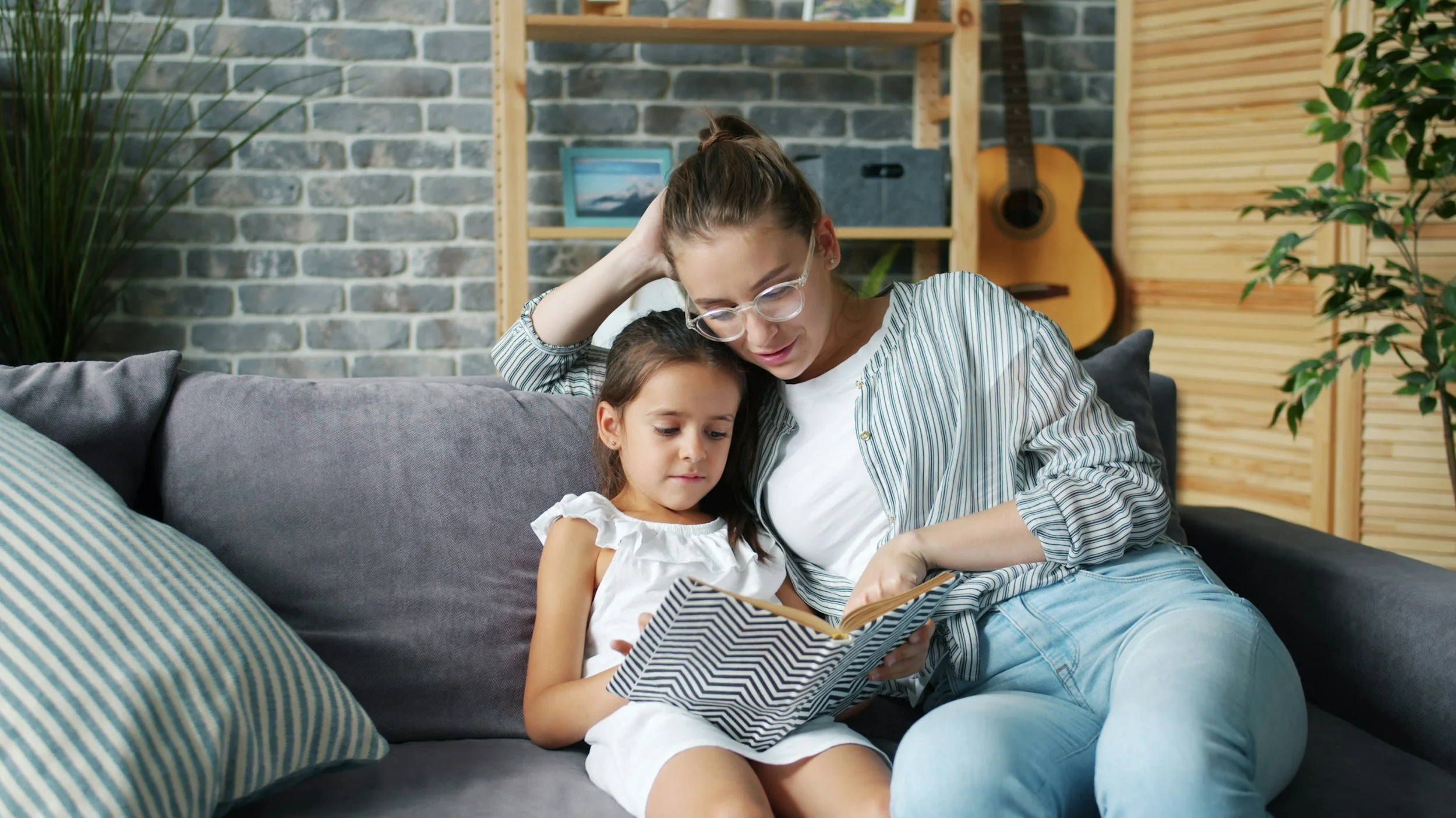 Parent reading a book to a child on a couch.