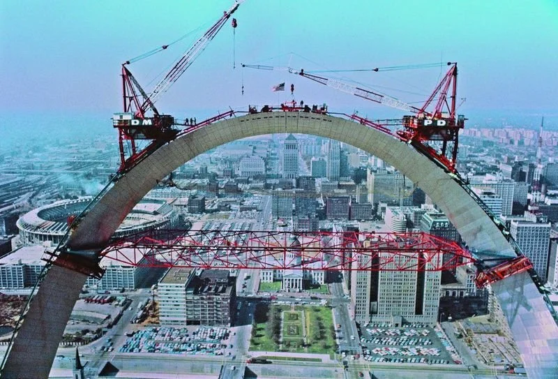 Construction cranes placing the final section of the Gateway Arch in St. Louis with downtown city skyline in the background