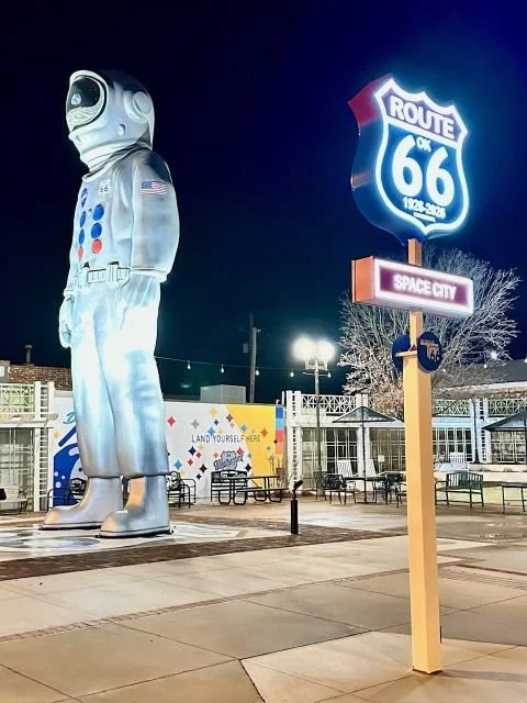 Nighttime view of Space City Park in Weatherford, Oklahoma on Route 66, showing a large spaceman statue and an illuminated Space City sign.