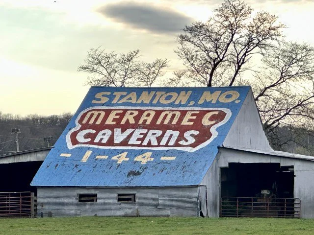 A roadside barn with a large Meramec Caverns advertisement painted across the roof, visible from the highway.