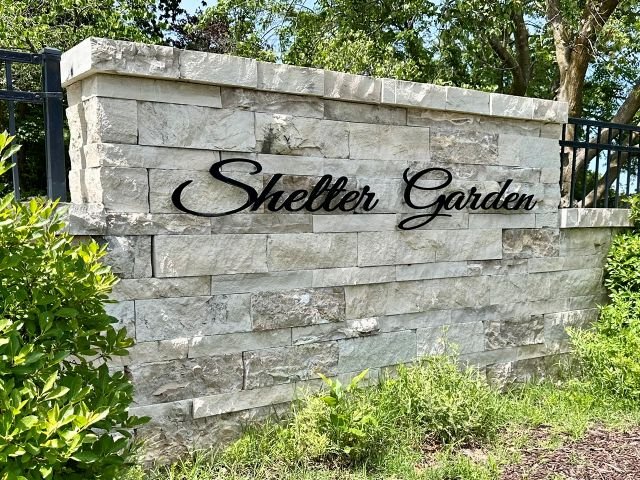Stone entrance sign for Shelter Gardens in Columbia, Missouri, surrounded by landscaping and greenery