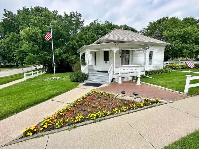 White house in Winterset, Iowa where John Wayne was born, shown with flowers planted in front and a simple, historic exterior.