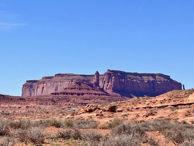 Large sandstone buttes in Monument Valley, Arizona, surrounded by a vast desert landscape under sunny skies.