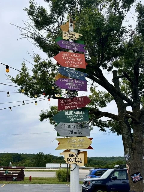 Tall signpost at Uranus Fudge Factory in Missouri featuring multiple destination signs that point toward cities and landmarks with their distances, creating a fun roadside photo opportunity.