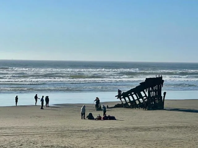 Wreck of the Peter Iredale ship on a sandy beach with the Pacific Ocean behind it near Astoria, Oregon.