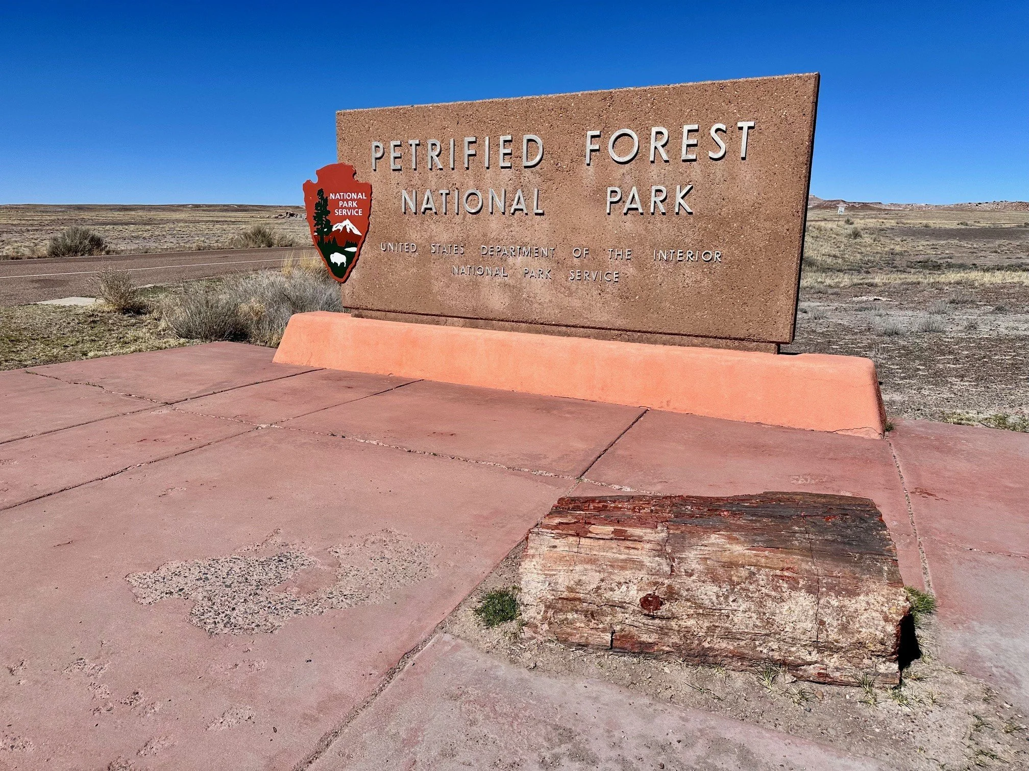 Petrified Forest National Park entrance sign with a large petrified log resting in front of it, marking the start of a colorful desert adventure.