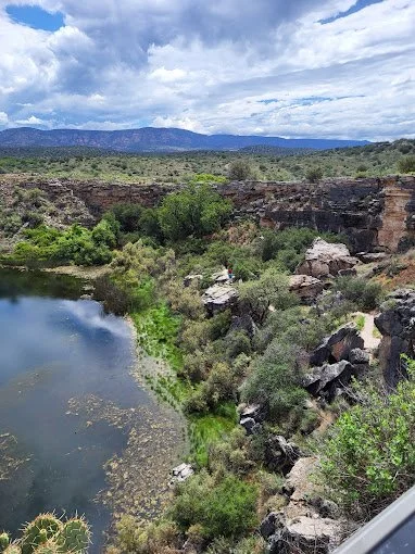 Beaver Creek flowing through Montezuma Castle National Monument in Arizona, bordered by lush greenery and desert canyon walls beneath ancient Sinagua cliff dwellings