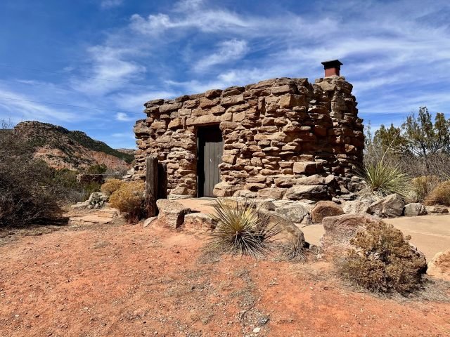 Rock Cow Cabins sitting on the floor of Palo Duro Canyon with a prominent butte visible in the background in Texas.