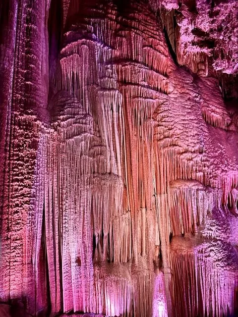 A 70‑foot limestone “Stage Curtain” formation inside the Meramec Caverns Theatre Room, highlighted by lighting that emphasizes its tall, rippling mineral columns.