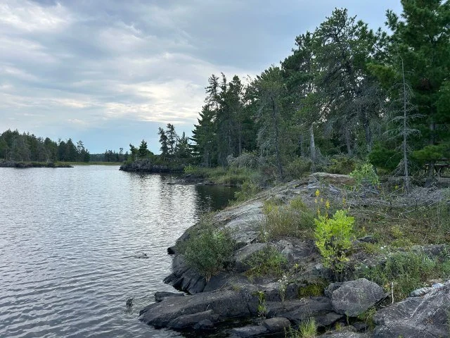 Rocky shoreline of Rainy Lake in Voyageurs National Park under clear blue skies, ideal stop for an EV road trip through Minnesota wilderness.
