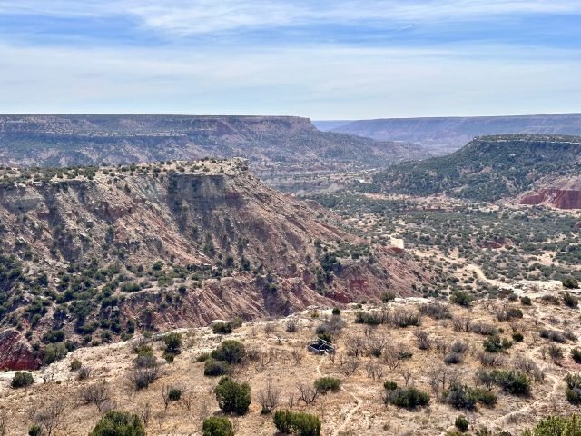 View of Palo Duro Canyon with layered red and orange cliffs stretching into the distance, while the CCC Trail winds through the rocky terrain in the foreground.