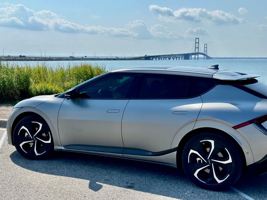 GrayKia EV6 parked beside Lake Michigan with the Mackinac Bridge in the distance during a 2024 electric vehicle road trip exploring Michigan's Great Lakes region and scenic coastal routes.