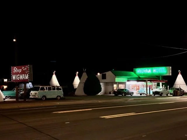 Nighttime photo of the Wigwam Motel in Holbrook, Arizona on Route 66, showing illuminated concrete wigwam rooms under the dark sky.